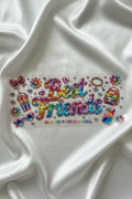 A sheet of colorful, iridescent rhinestone stickers featuring the phrase 'Best Friends' in large script, surrounded by small charms, hearts, and floral designs, laid flat on a white fabric background.
