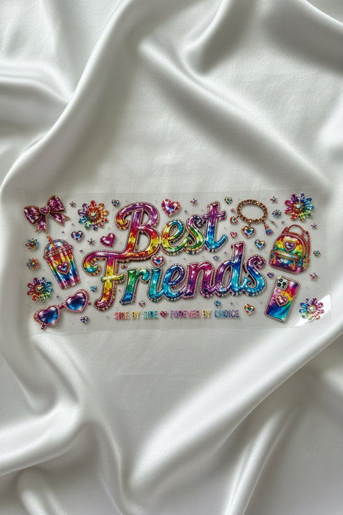 A sheet of colorful, iridescent rhinestone stickers featuring the phrase 'Best Friends' in large script, surrounded by small charms, hearts, and floral designs, laid flat on a white fabric background.
